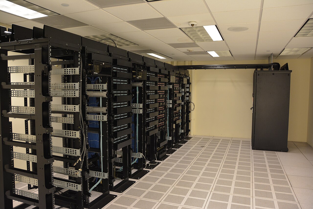 Rækker af serverracks i et datacenter med hævet gulv og lysstofrør i loftet
